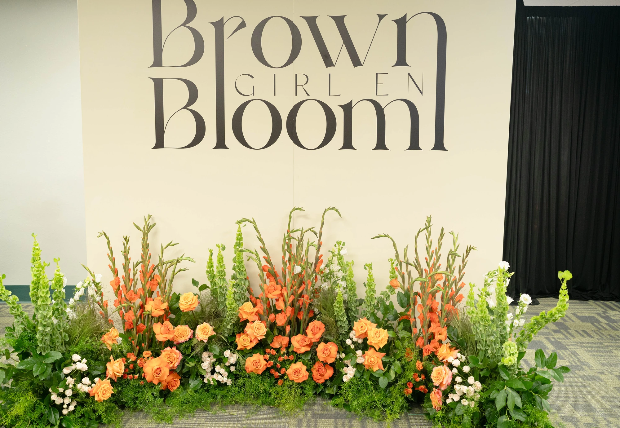 Orange florals beneath the Brown Girl en Bloom branded backdrop