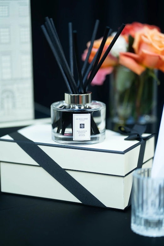 Jo Malone fragrance diffuser and ribboned gift boxes beside orange roses