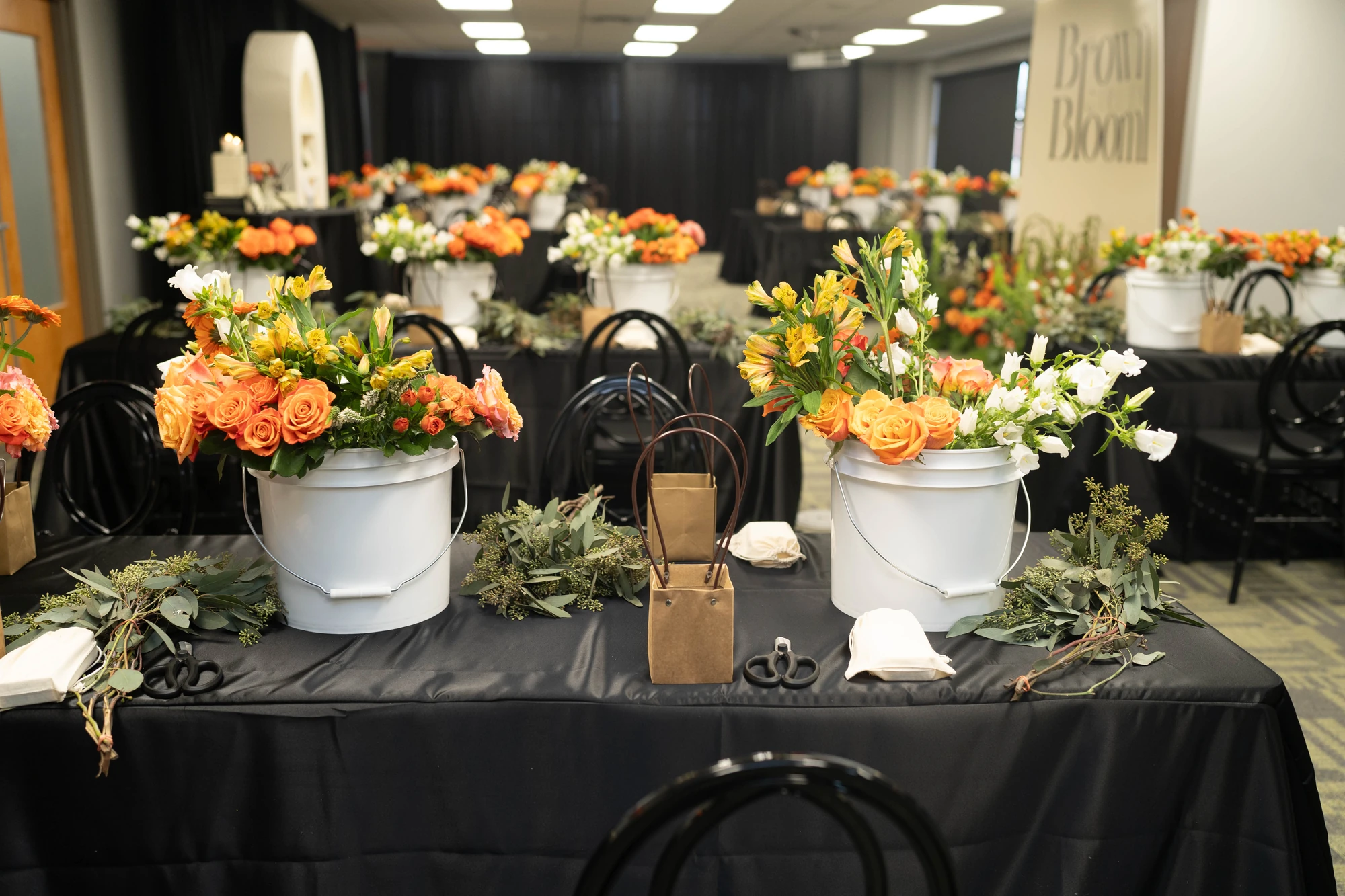 A floral workshop setup with black tables and branded flower buckets